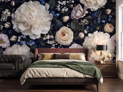 Ivory peonies on deep blue-black wallpaper behind a low bed with an olive throw and a gold lamp