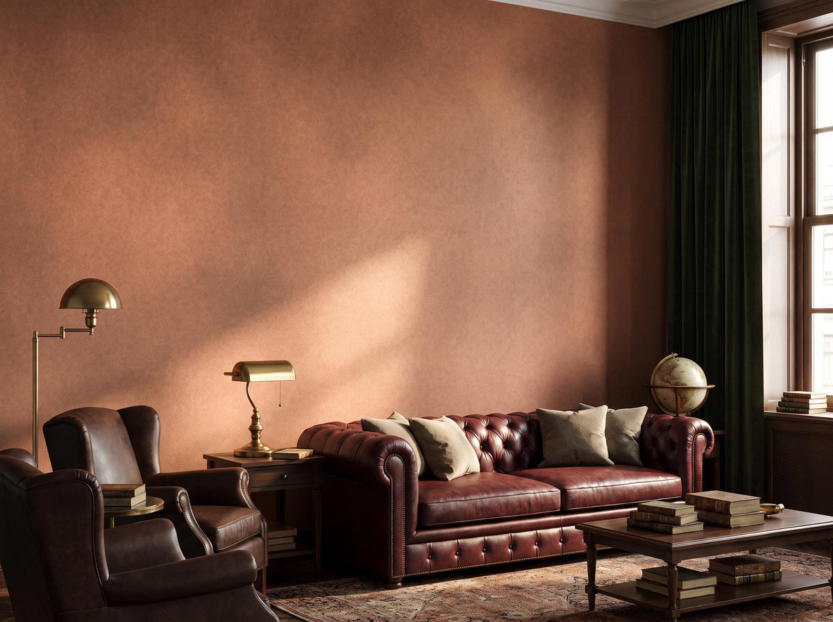 Rust limewash wall catching daylight, with an oxblood leather sofa and a brass desk lamp