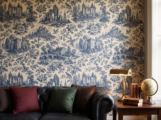 Blue engraved toile wallpaper behind a dark leather chesterfield sofa, brass lamp and globe